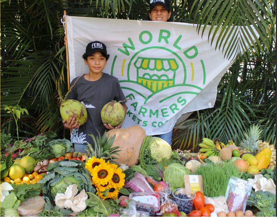 Niño y voluntaria de la FeriaMX con la bandera de la World Farmers Markets Coalition