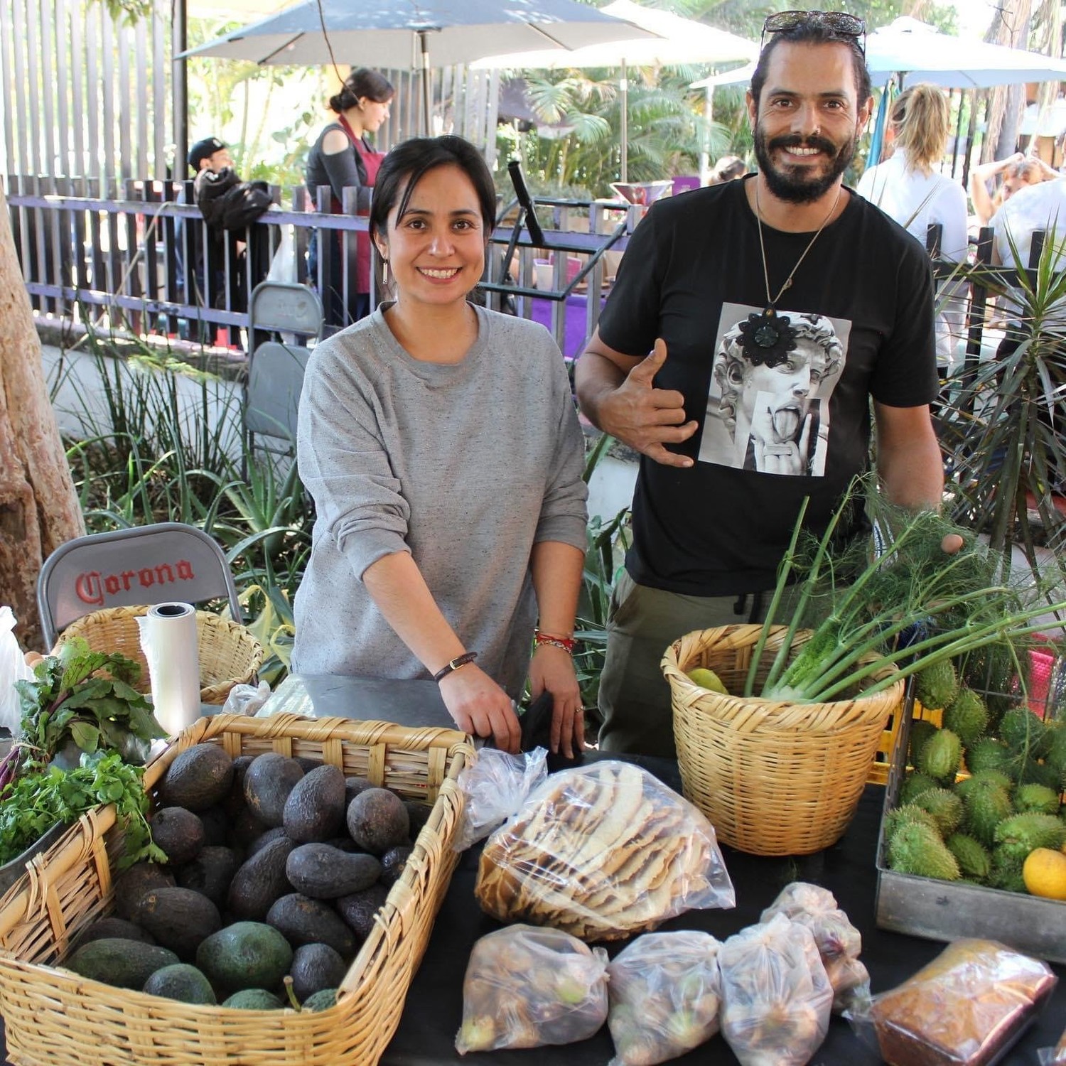 Pareja de productores de Acampo en su puesto, con canastas de aguacate, tortillas y hierbas frescas