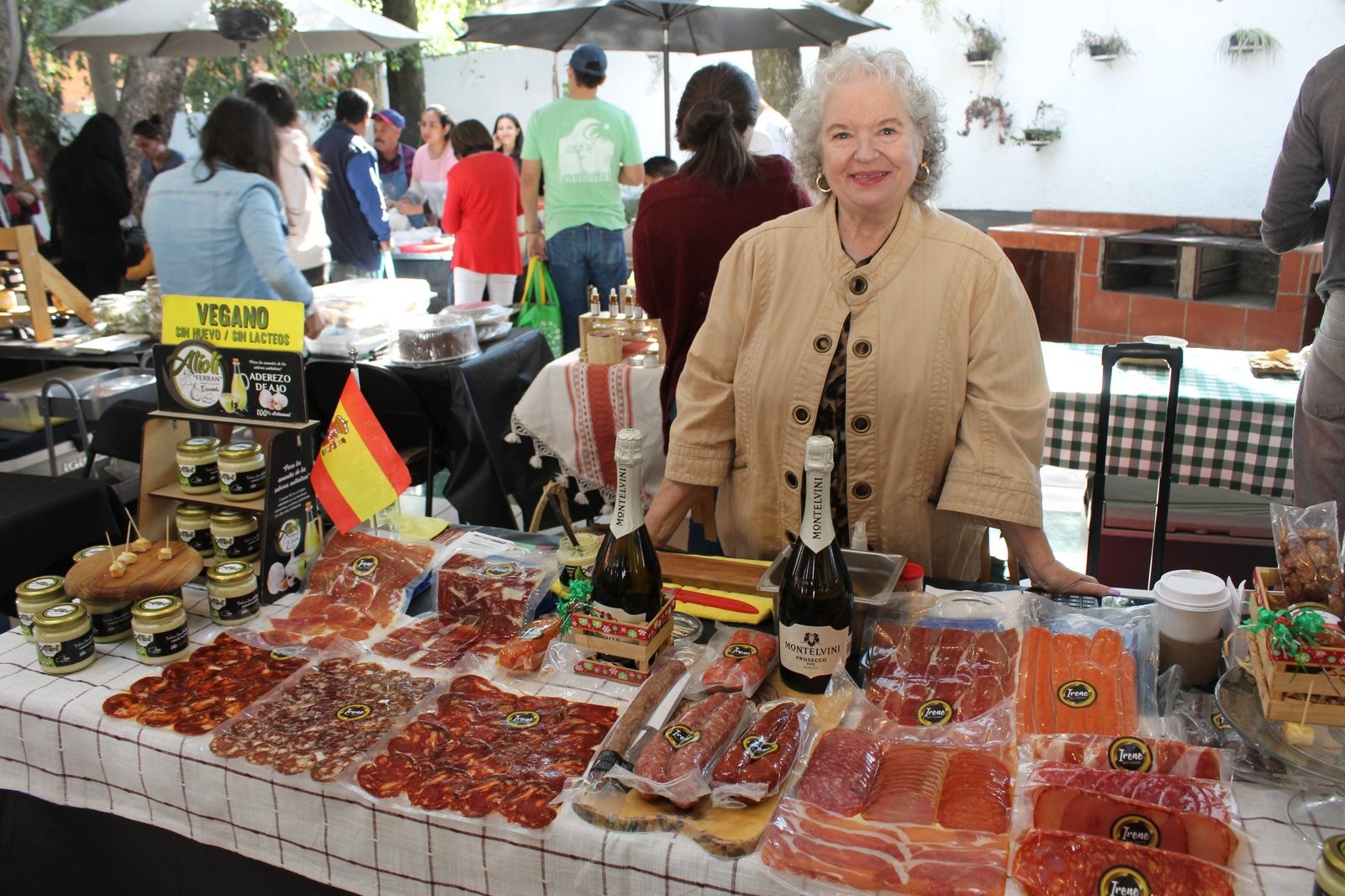Mujer en el puesto de Aioli de Ferrán, con letrero de alioli vegano, bandera de España y charolas de embutido