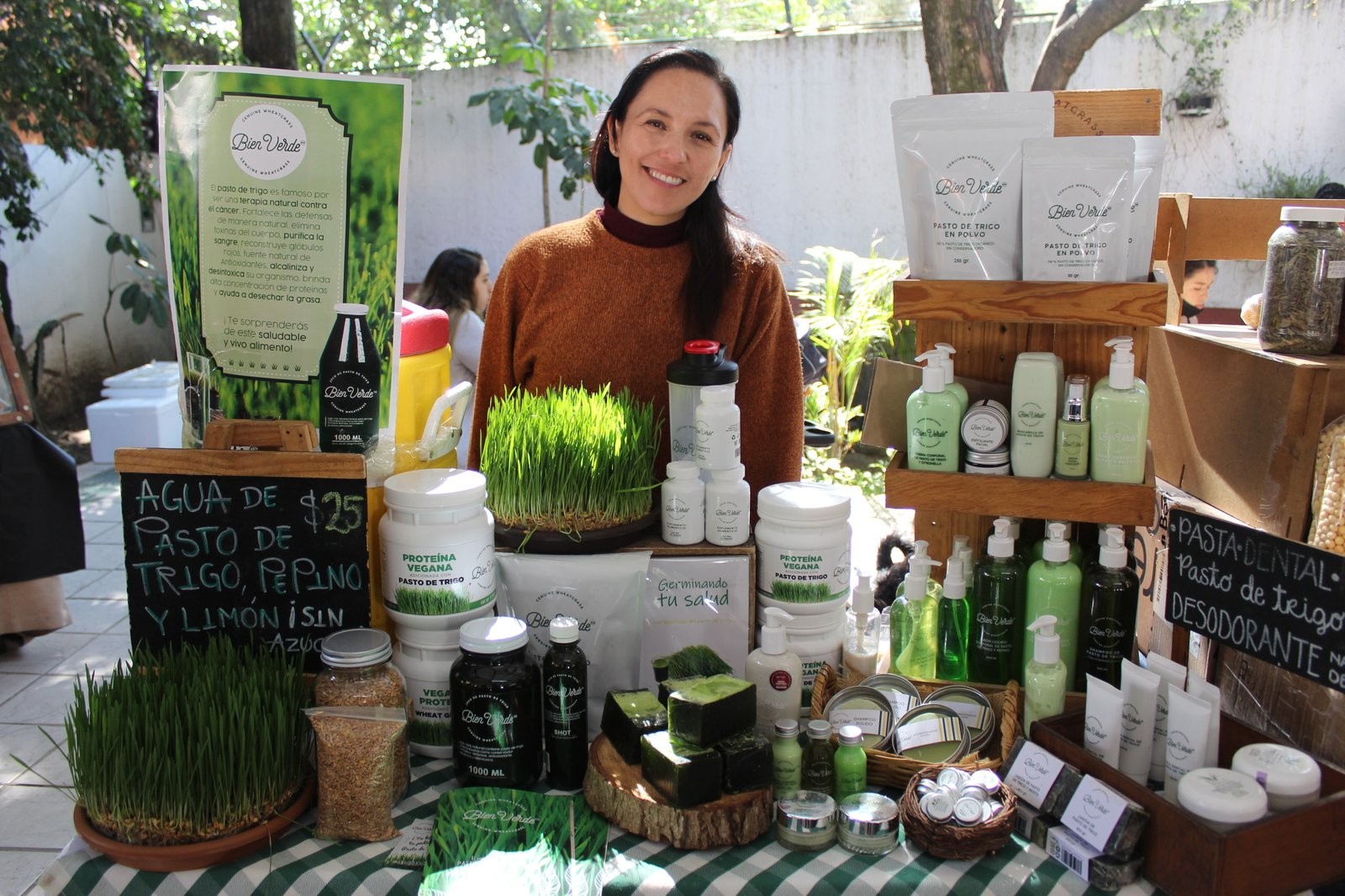 Responsable de Bien Verde en su puesto, con pasto de trigo vivo, polvos, jugos y la línea de cosmética