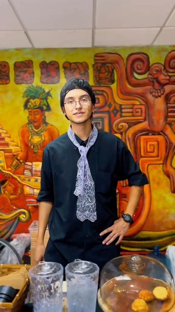 Integrante del equipo de Café Catrina en la tostaduría, frente a un mural de arte mesoamericano