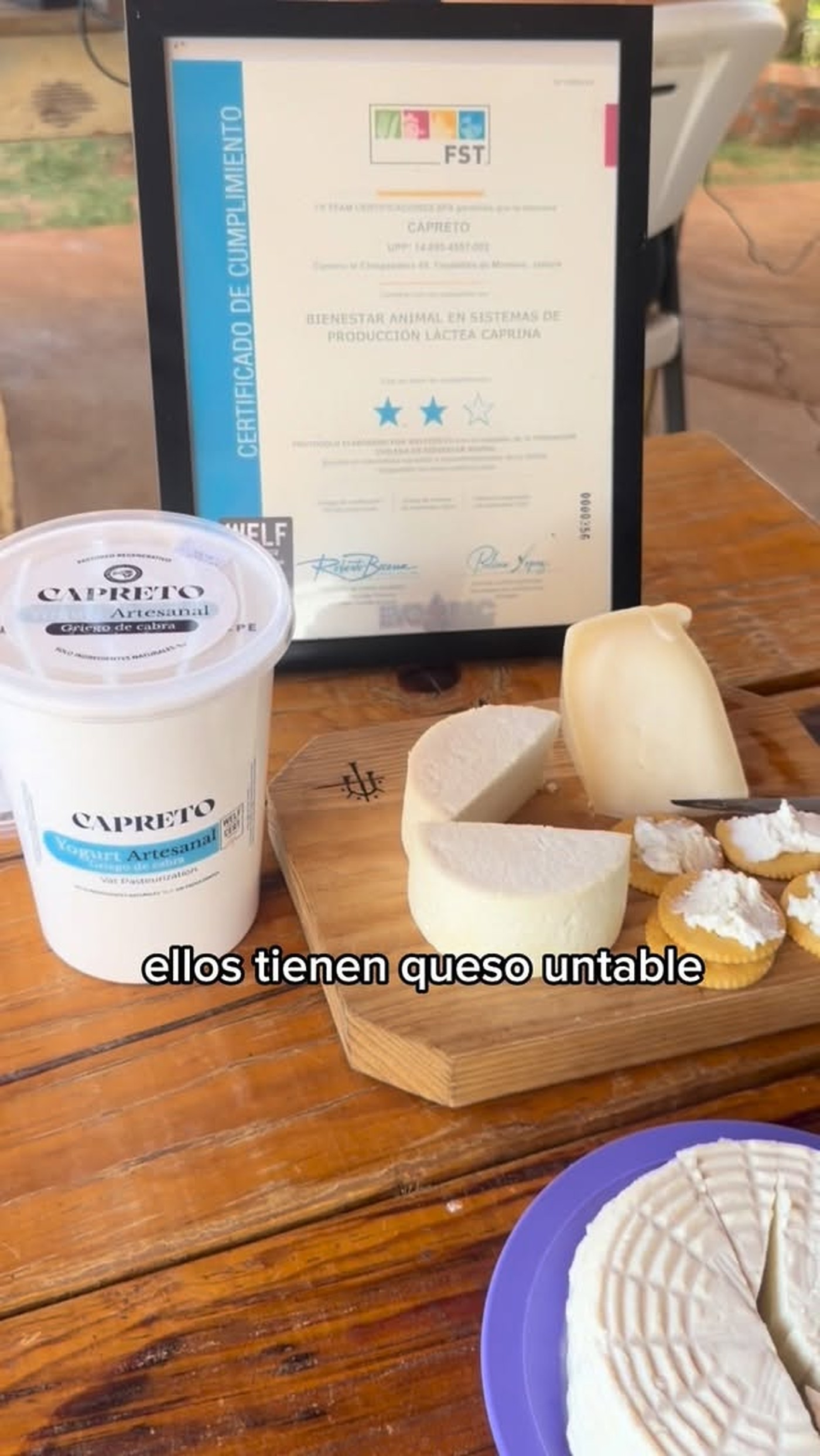 Yogurt y queso de cabra artesanal de Capreto sobre una tabla de madera, junto al certificado de Bienestar Animal FST