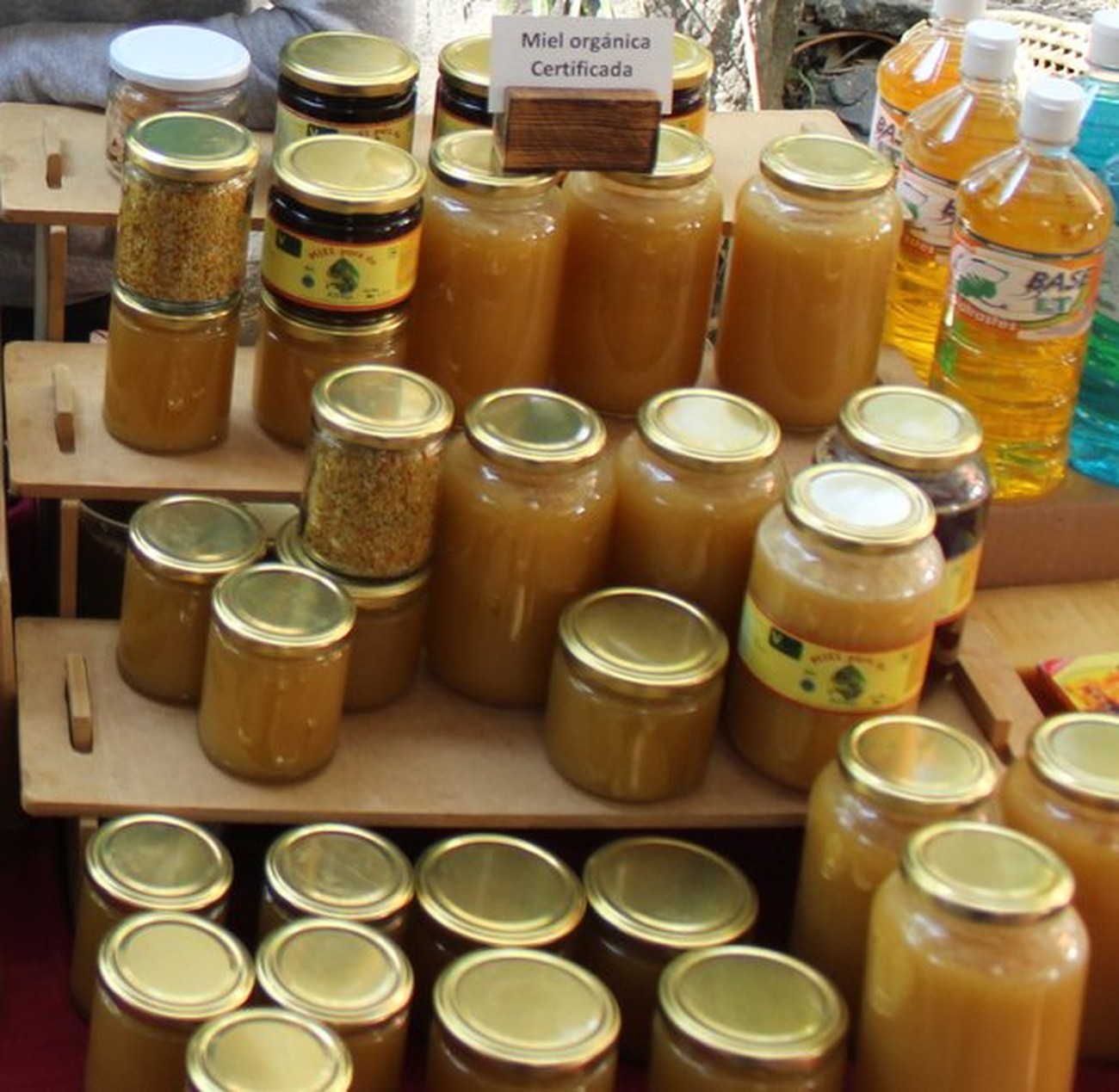 Frascos de miel orgánica certificada de Cooperativa Niyama apilados en un exhibidor de madera, junto a polen y aceites