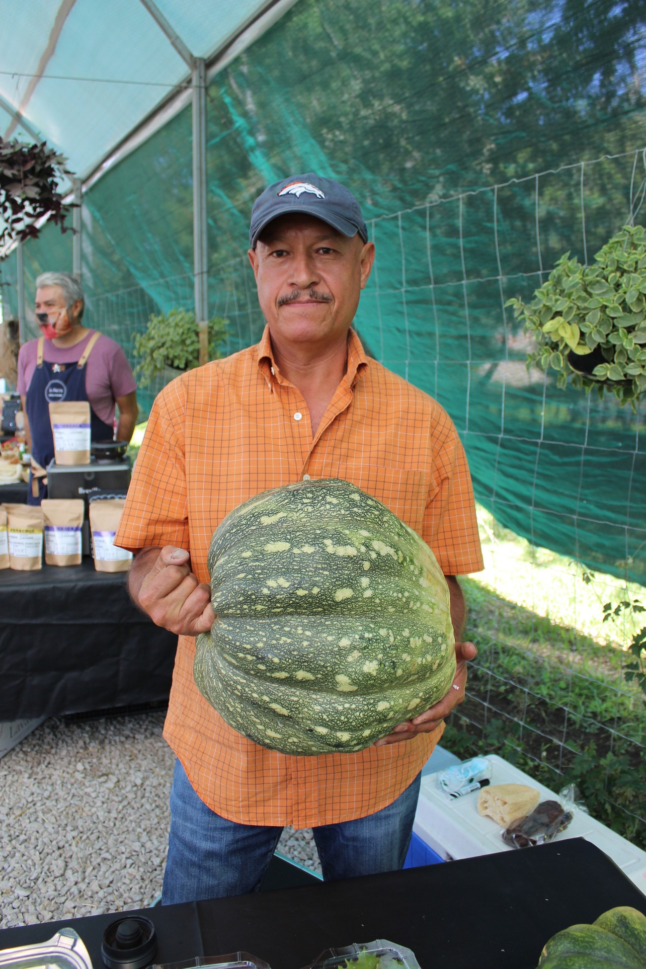 Productor de Granja El Colibrí sosteniendo una calabaza grande de temporada bajo un invernadero