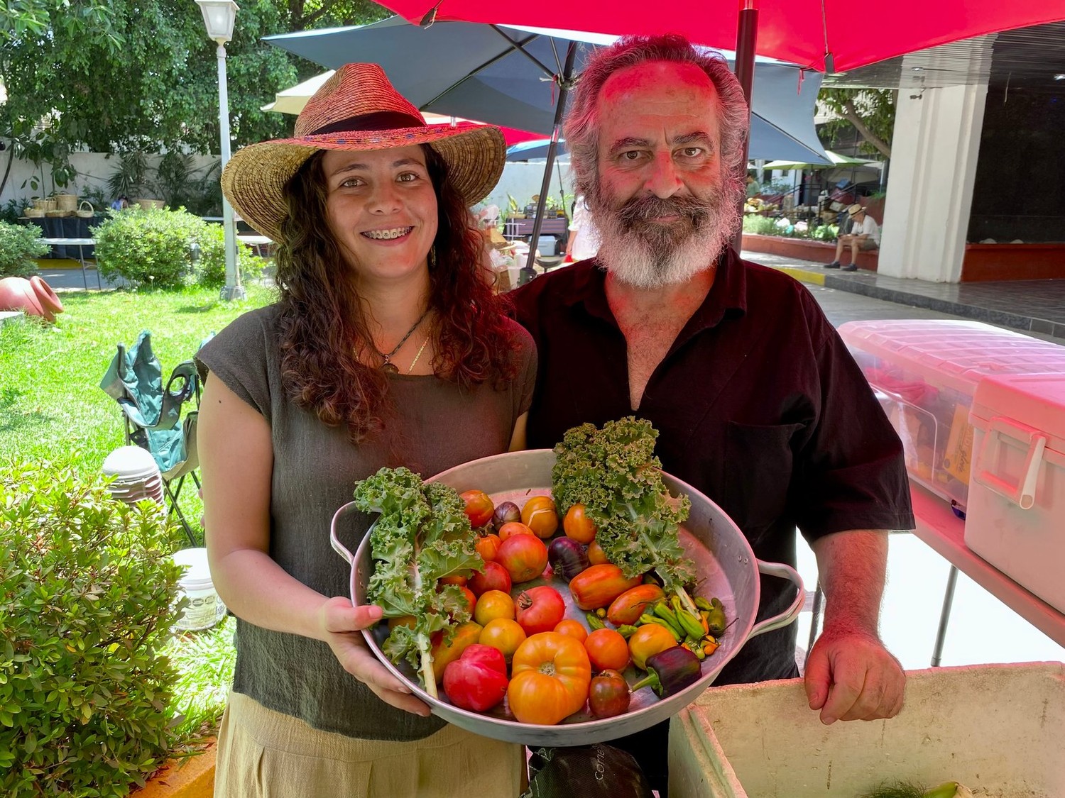 Los dos productores de Huerto Los Guayabos sosteniendo una charola con jitomates criollos, kale y chiles
