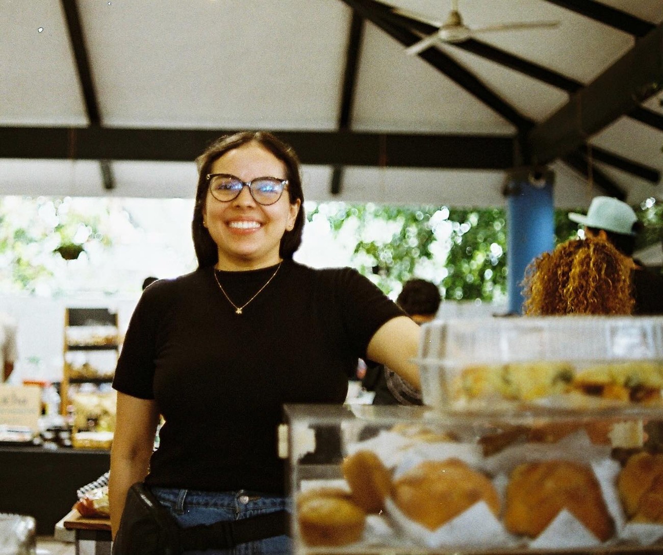 Retrato de la fundadora de Mikela's sonriendo junto a la vitrina de repostería del puesto
