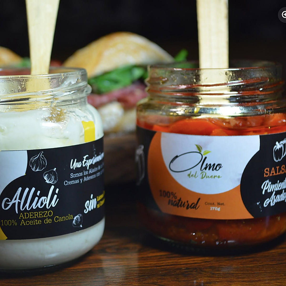 Frascos de allioli y salsa de pimientos asados de Olmo del Duero junto a un sándwich