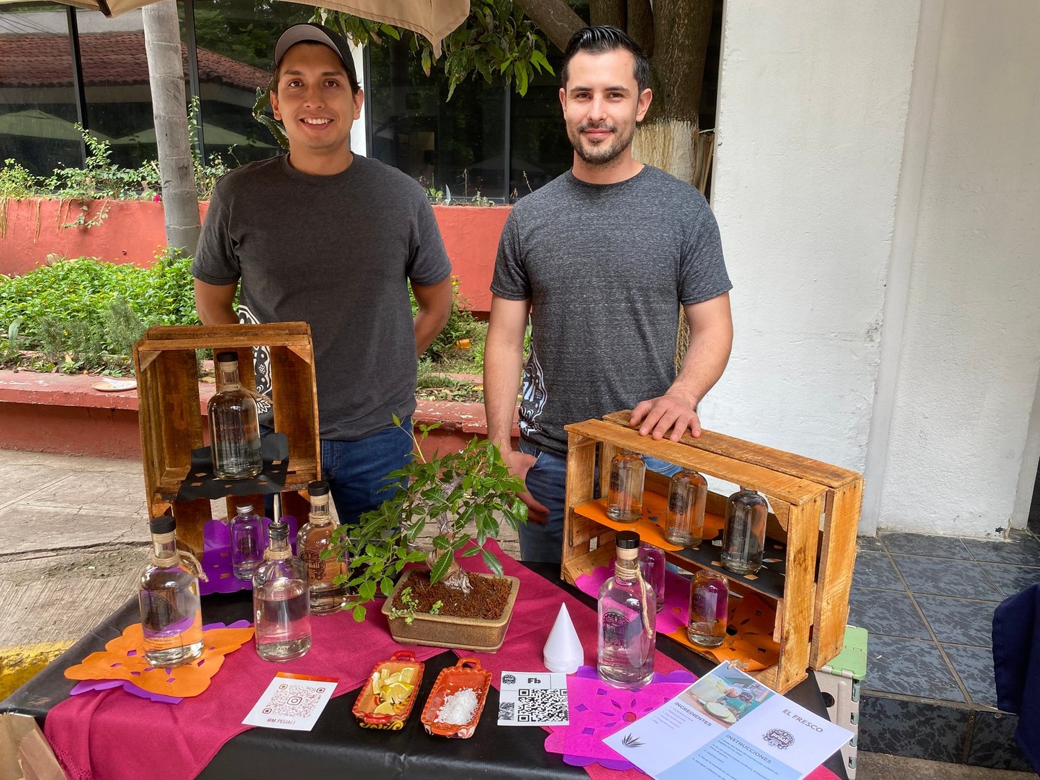 Los dos productores de Peuali detrás de su puesto, con botellas exhibidas en huacales de madera