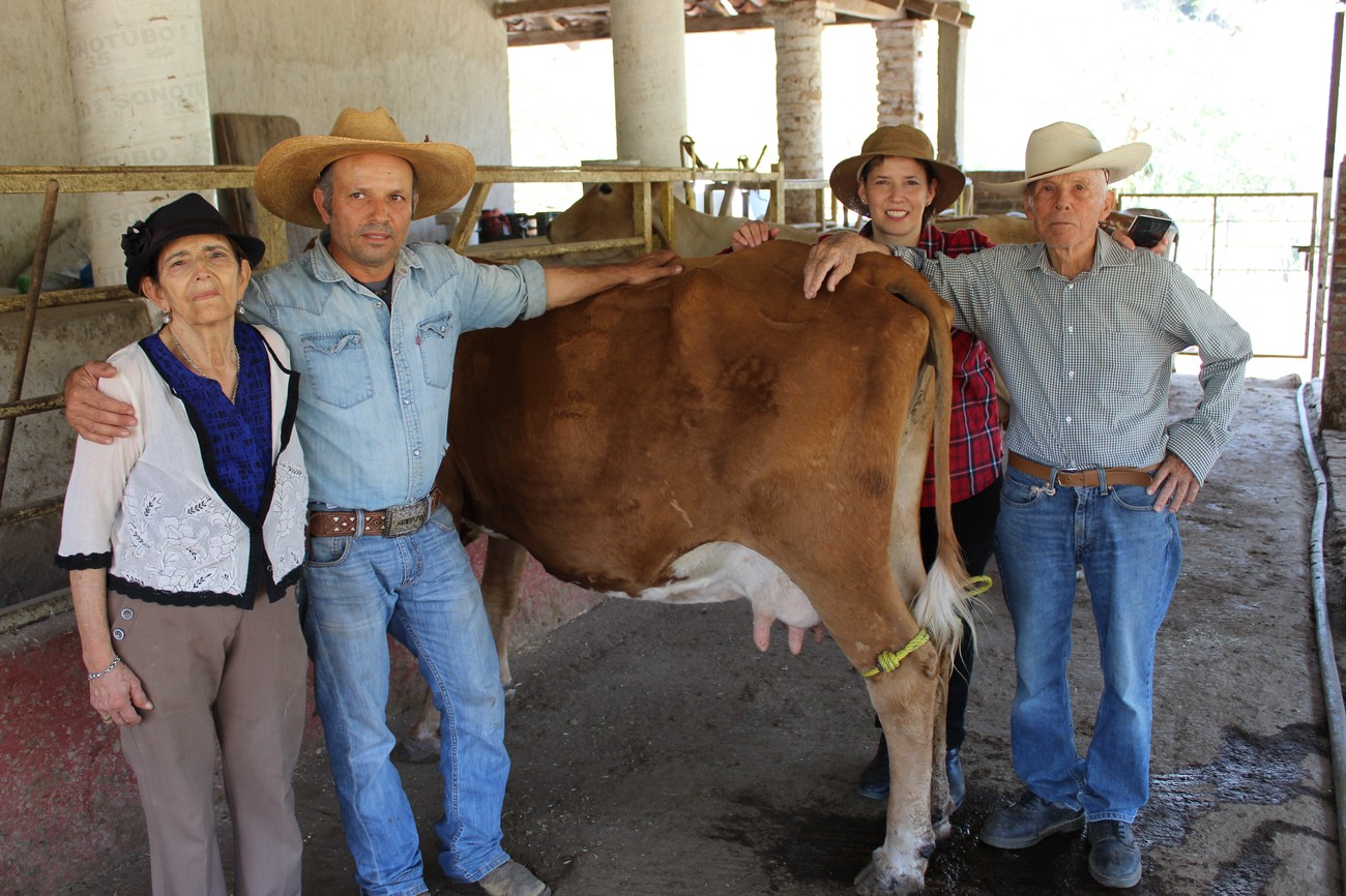 Tres generaciones de la familia de Rancho La Jabalina posando junto a una vaca lechera bajo un establo de columnas de piedra